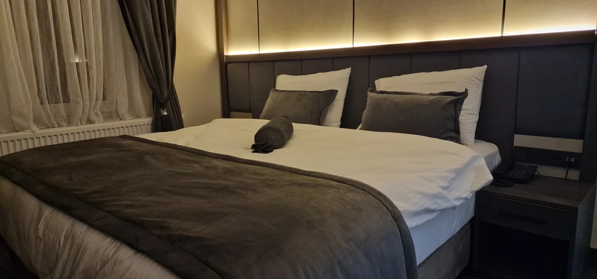 Doppelzimmer mit grauem Polsterkopfteil und indirekter Beleuchtung.
