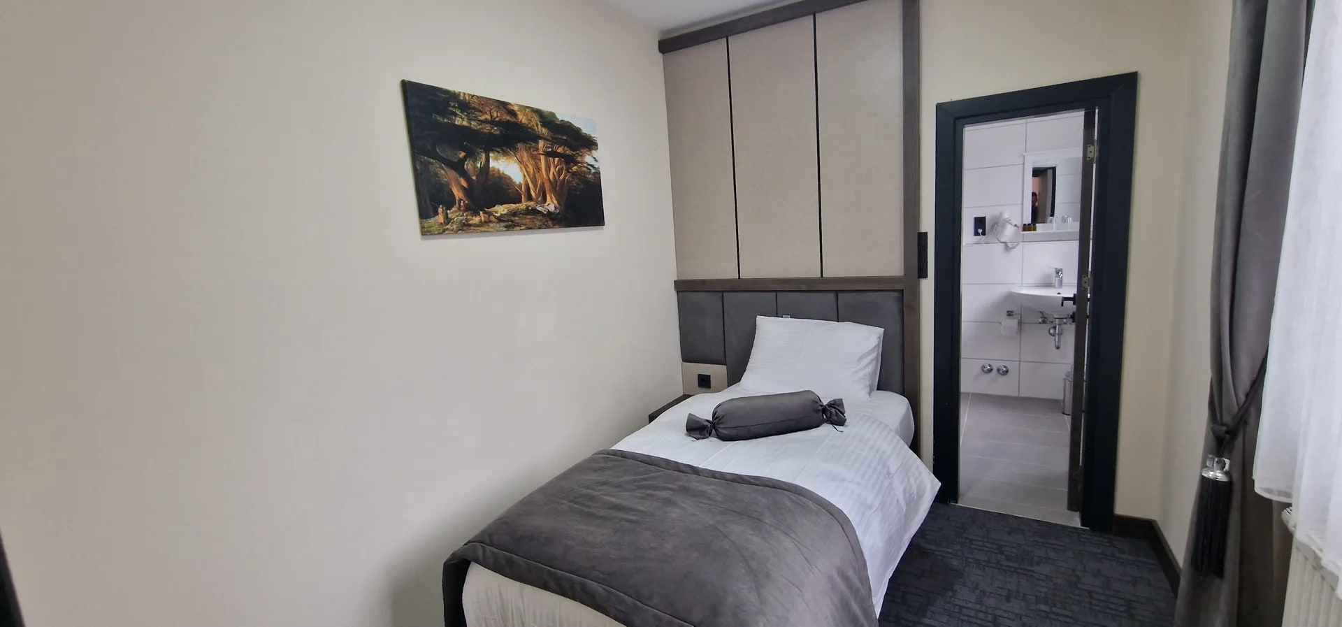 Einzelzimmer mit Wandbild und Blick ins Bad